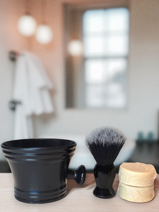 Shaving brush, black bowl, and soap on a bathroom counter with blurred background